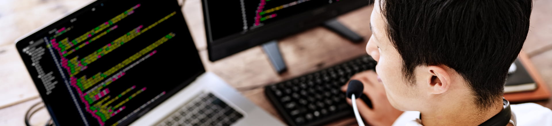 2台のモニターにコードを表示しながら作業するエンジニアの後ろ姿